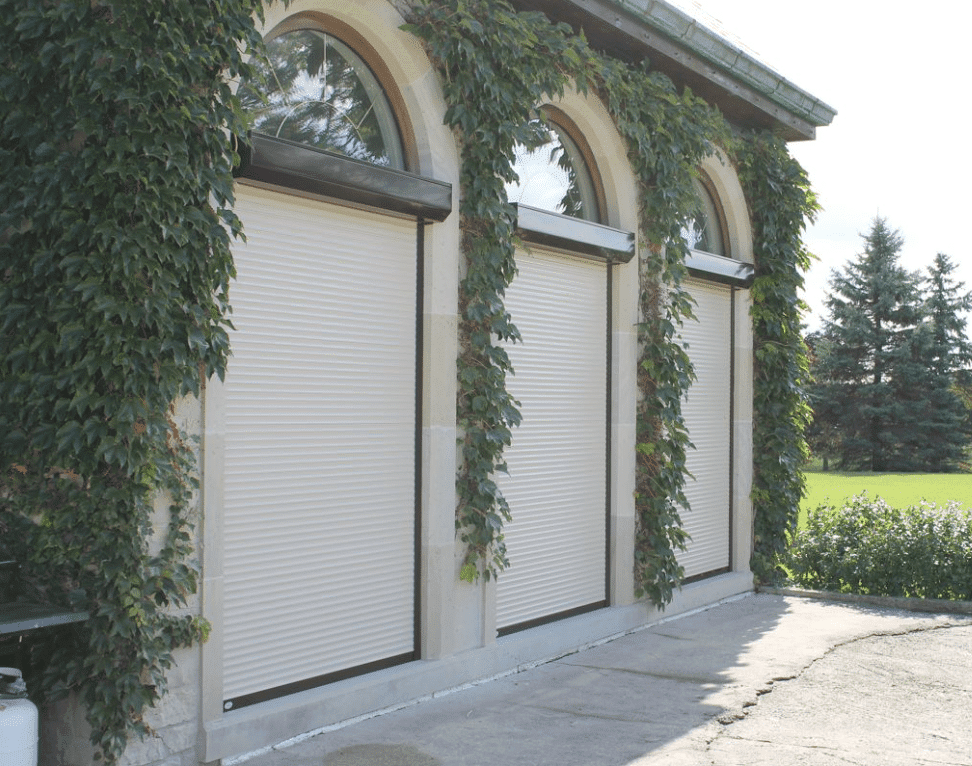 Cream roll-up shutters closed over three arched openings on an ivy-covered stone building
