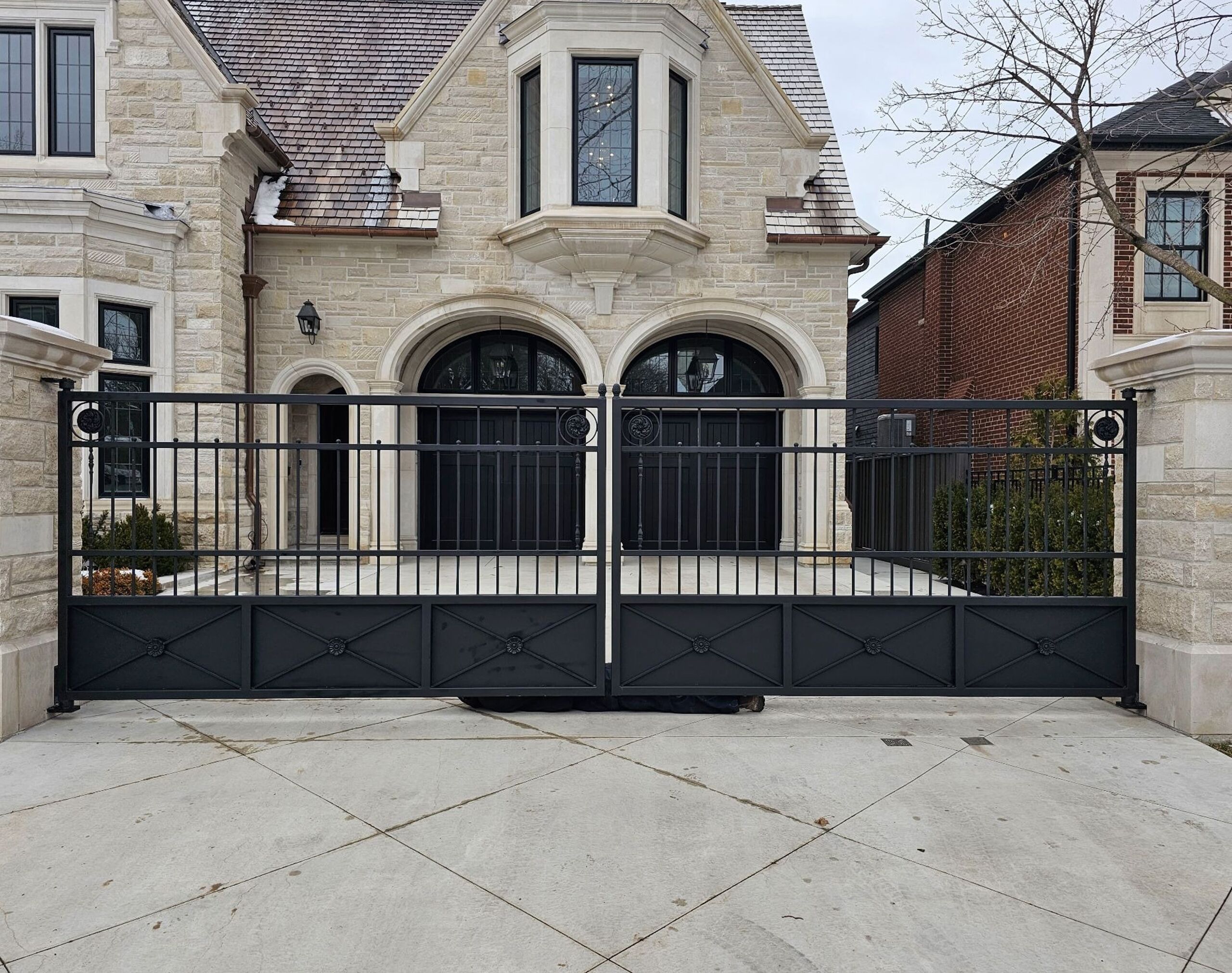 Modern black metal swing driveway gate at a residential entrance
